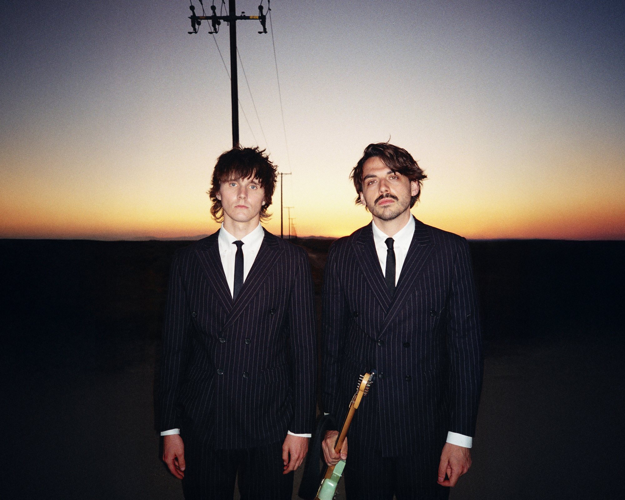 YES AND MAYBE in pinstripe suits at sunset, power lines running to the horizon behind them